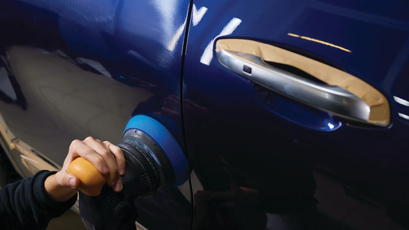 Machine polisher buffing a dark blue car door with the handle masked, from TGA's brand imagery